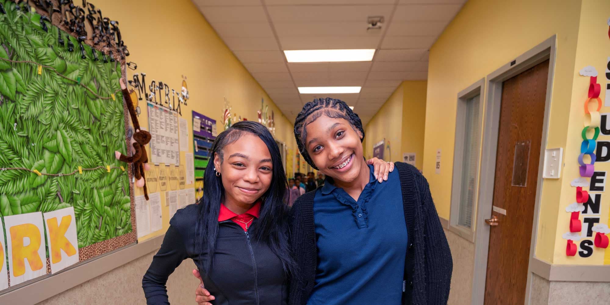 Two smiling people standing together in a school hallway.