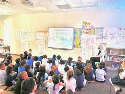 Adult reads to children seated on floor in classroom.