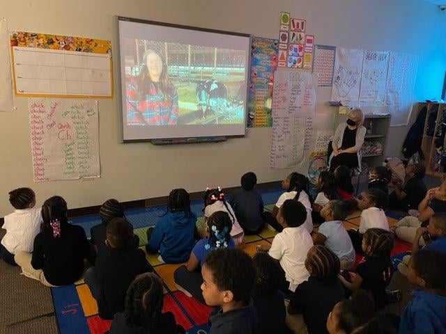 Children and an adult watch a video on a screen.