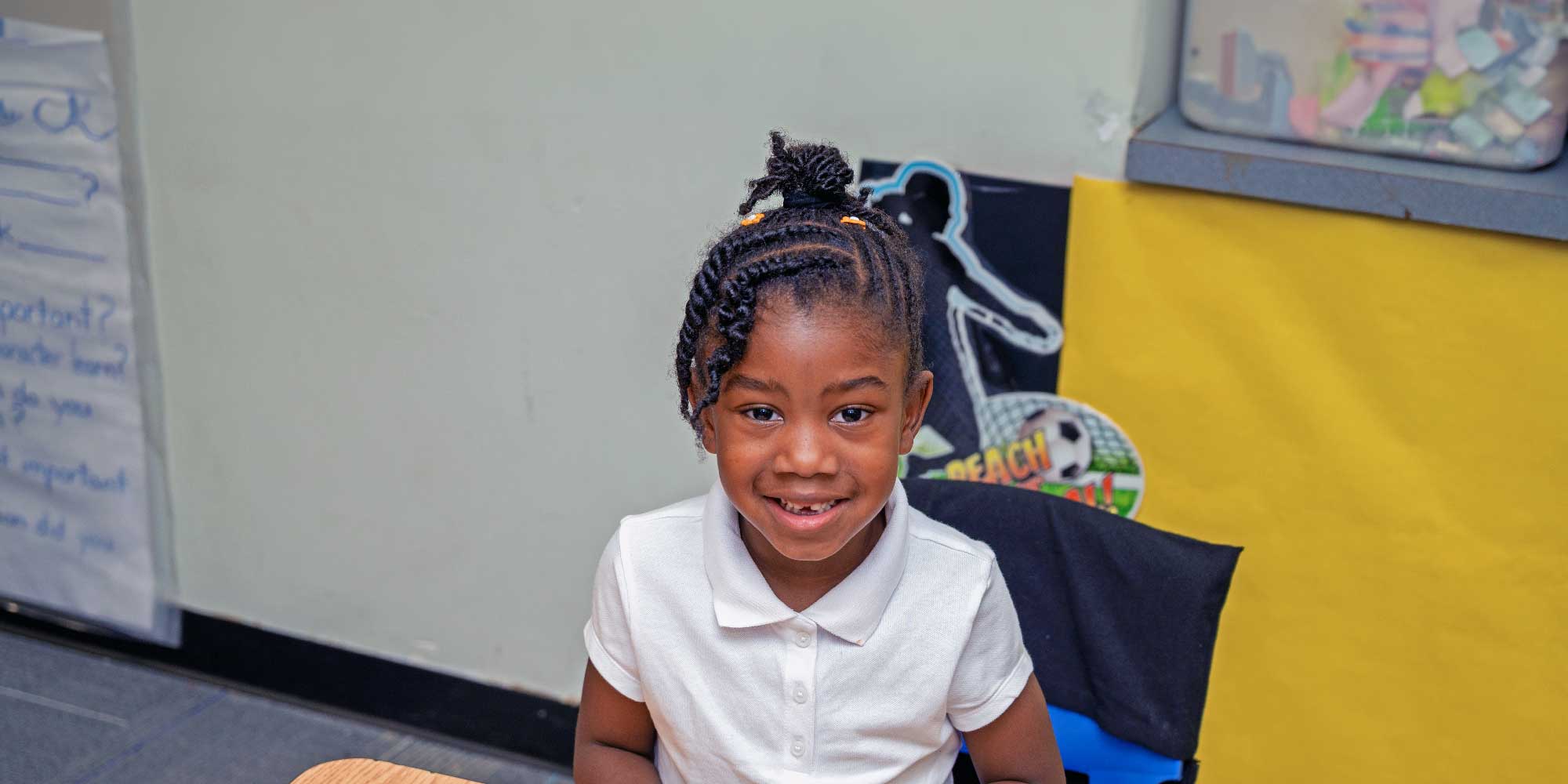 Smiling student in a white polo shirt in a classroom.